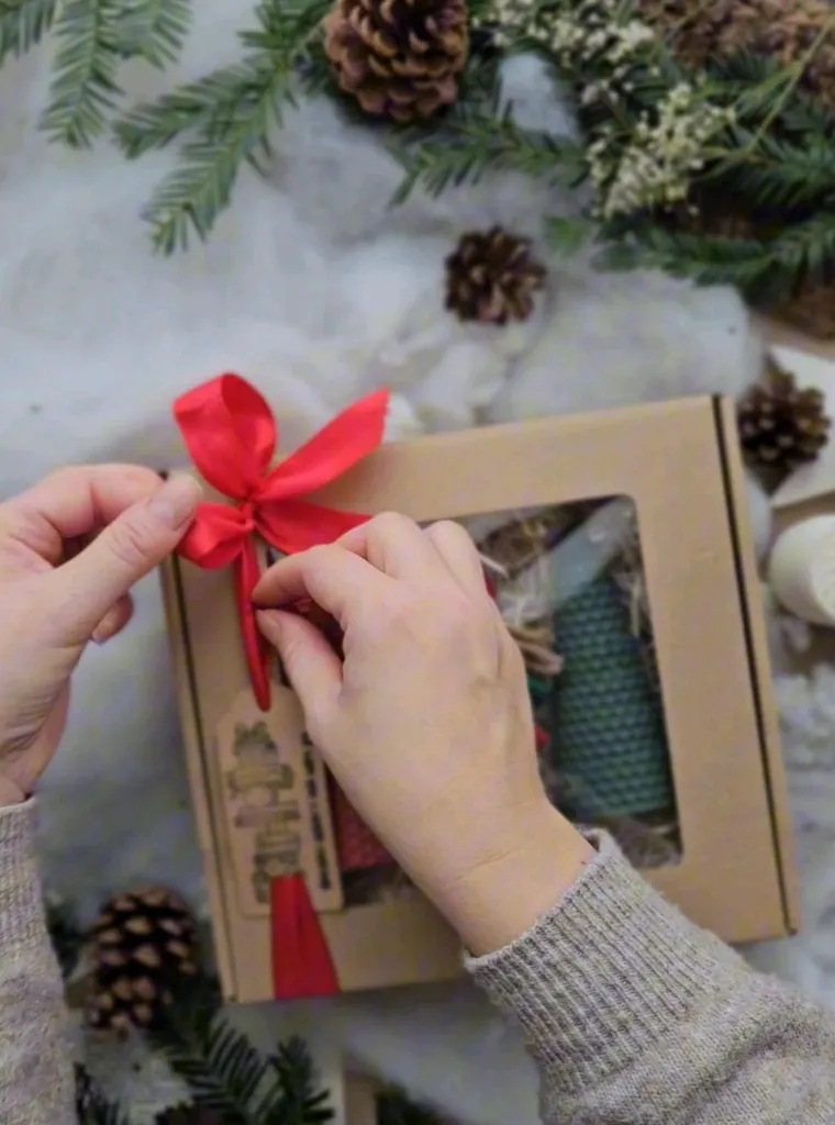 Tying a red ribbon on a boxed gift set with pine cones